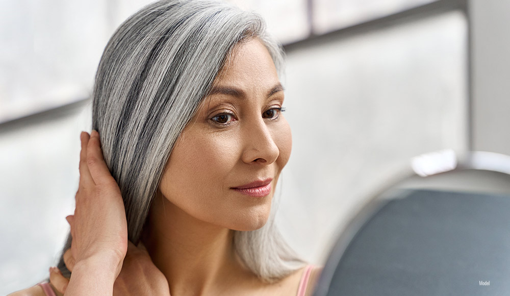 Portrait of a beautiful older woman with gray hair looking at herself in a mirror.