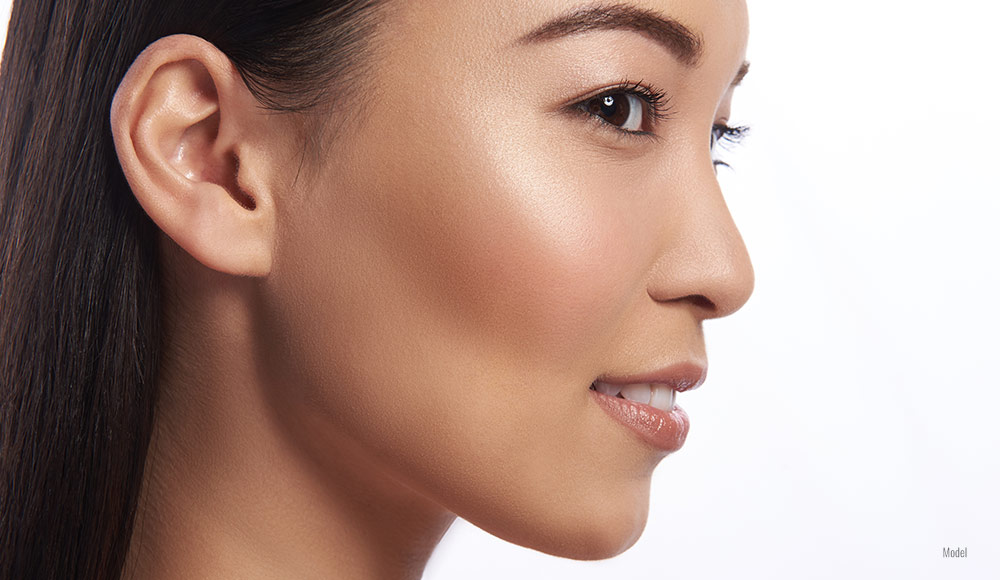 Close-up of a young woman from a side profile angle with her long hair tucked behind her ear.