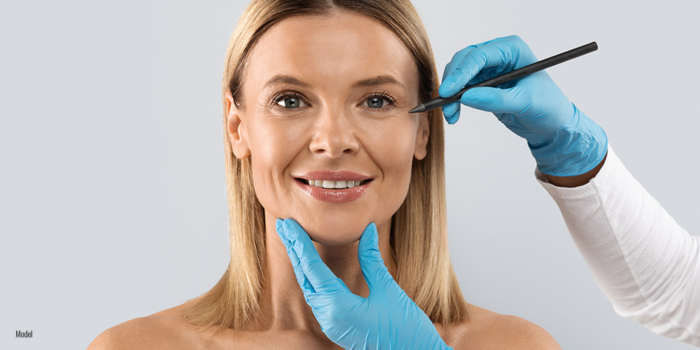 Woman smiling as someone with gloved hands marks her face with a pen